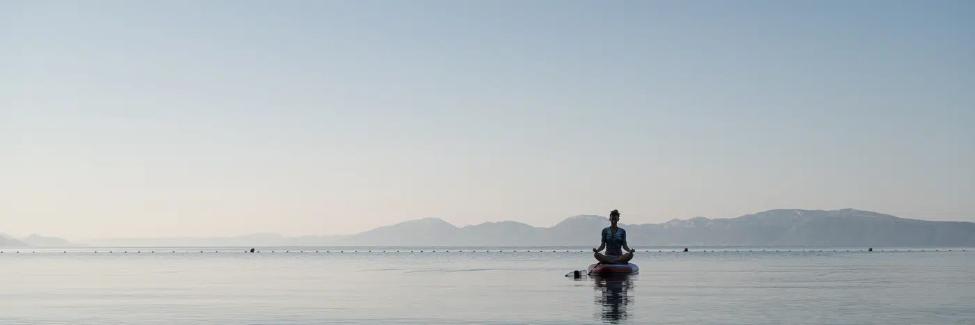 Person meditating peacefully over calm water at dawn