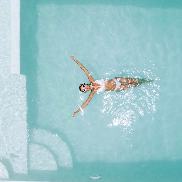 Woman relaxing in clear pool water in hot sunny day on Bali vill